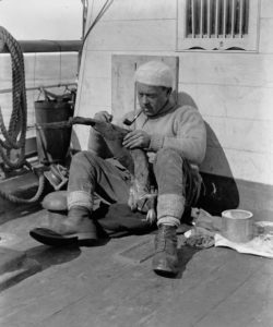 George Levick examinant une peau de manchot sur le pont du Terra Nova. Photo: Herbert Ponting, décembre 1910